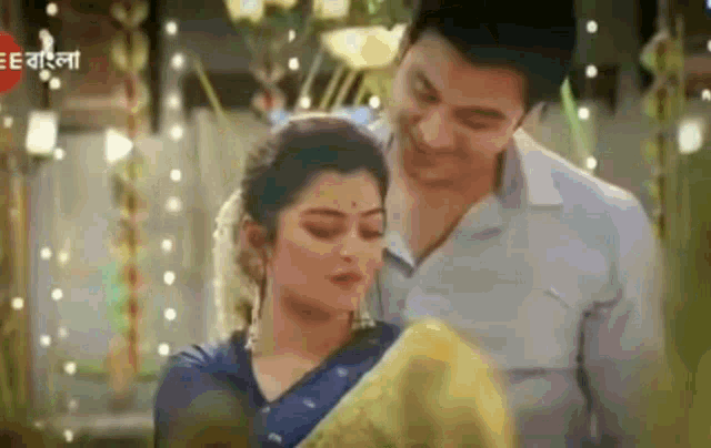 a man and a woman are standing next to each other . the woman is wearing a blue sari .