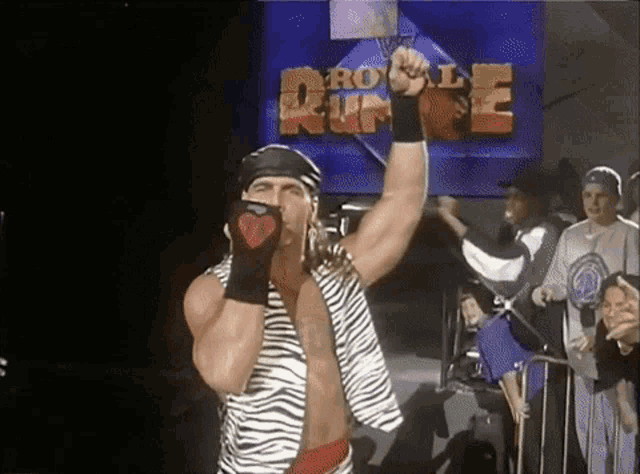 a man in a zebra print vest holds his fist in the air in front of a sign that says royal rumble