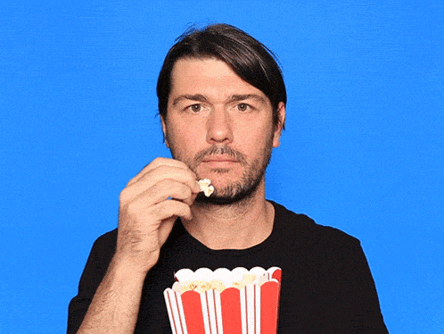 a man eating popcorn in front of a bucket of popcorn