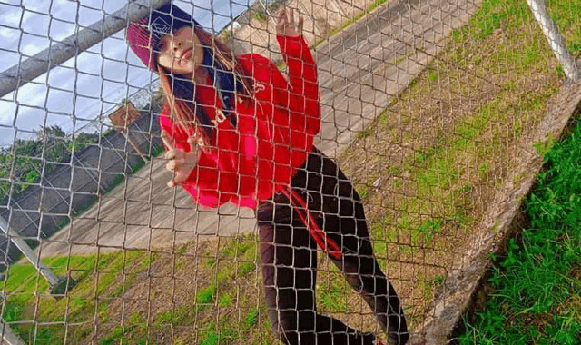 a girl in a red jacket and black pants is standing behind a chain link fence .