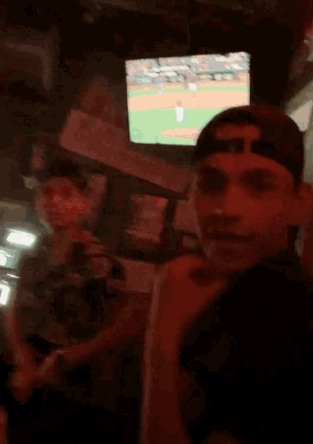 a man in a baseball cap stands in front of a baseball game on a television