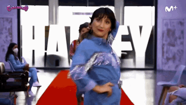 a woman in a blue dress is dancing on a red carpet in front of a sign that says haley
