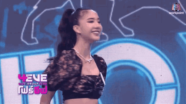 a woman in a crop top is smiling in front of a sign that says eve on it