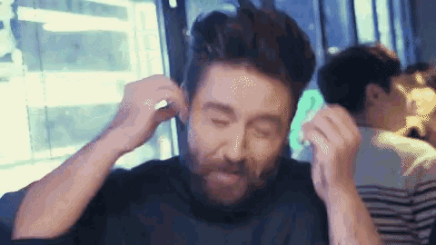 a man with a beard is covering his ears with his hands while sitting at a table .
