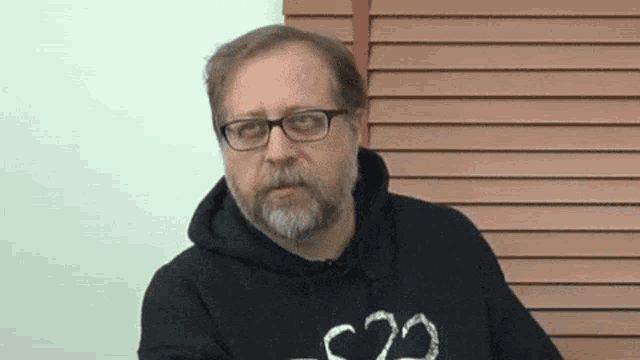 a man with glasses and a beard is wearing a black hoodie that says c22