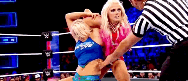 two women are wrestling in a ring and a referee is watching .