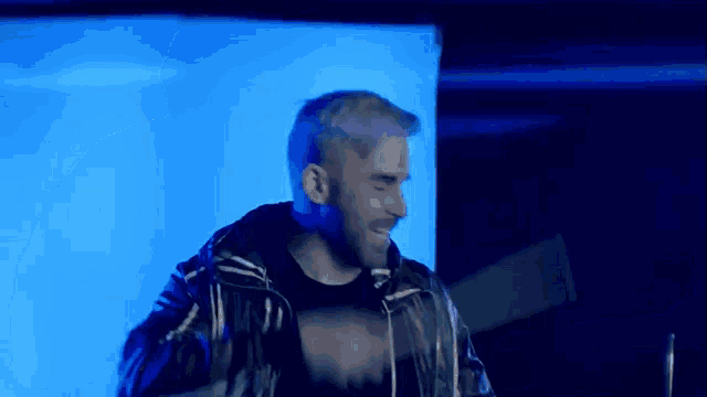 a man in a black jacket is dancing in front of a blue wall .