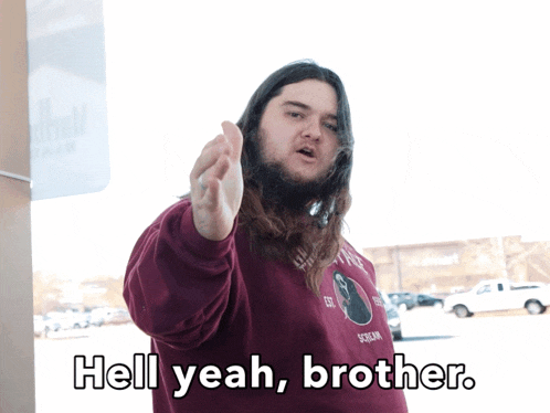 a man with long hair and a beard is pointing at the camera and says hell yeah brother