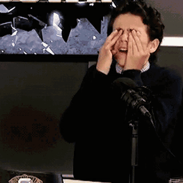 a man is covering his face with his hands while sitting in front of a microphone