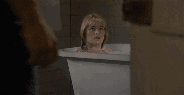 a woman is taking a bath in a bathtub and looking out the window .
