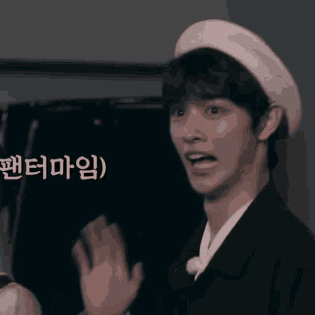 a man wearing a white hat and a black jacket is waving his hand