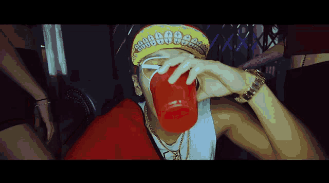 a man wearing a red cup and a bandana with gold teeth is drinking from it