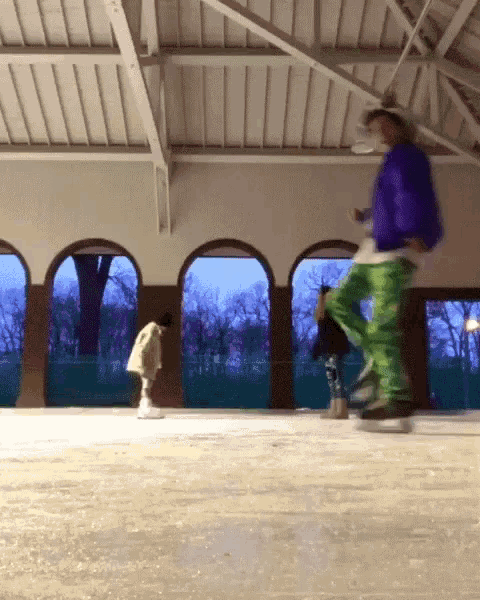 a man in a blue jacket and green pants is skating on a rink
