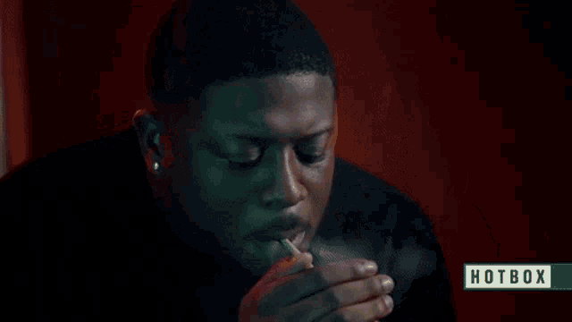 a man is smoking a cigarette with smoke coming out of his mouth and a hotbox logo in the corner .