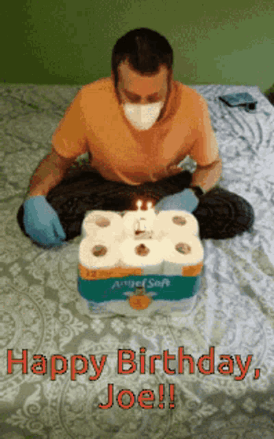 a man wearing a mask and gloves is sitting on a bed with a birthday cake made out of toilet paper