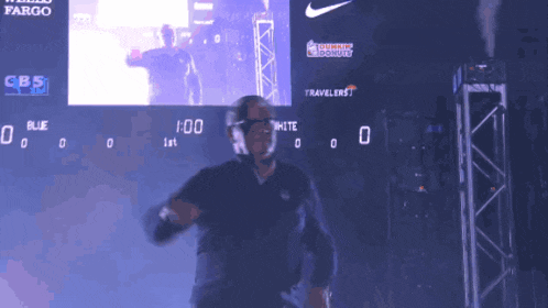a man stands in front of a scoreboard that says cbs and dunkin donuts