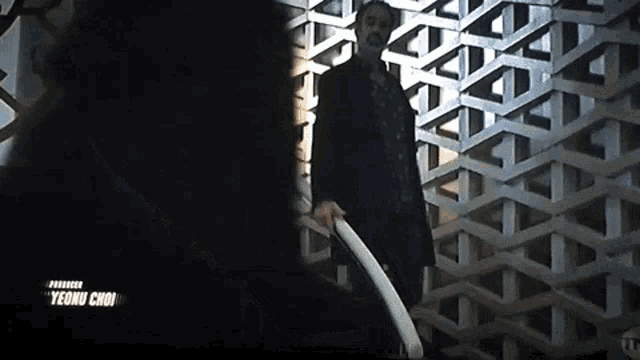 a man in a black coat is standing in front of a wall holding a sword .