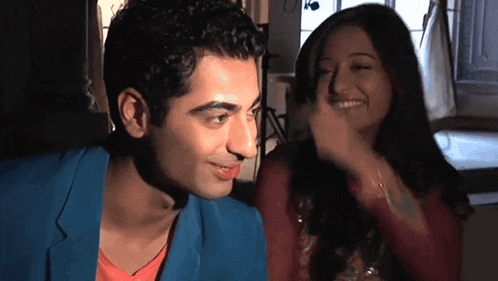 a man in a blue jacket and a woman in a red shirt are looking at each other and smiling