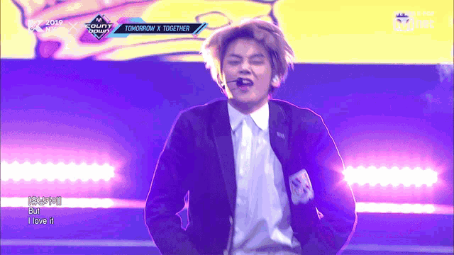 a man in a suit and tie performs on a stage with the words tomorrow x together on the screen behind him