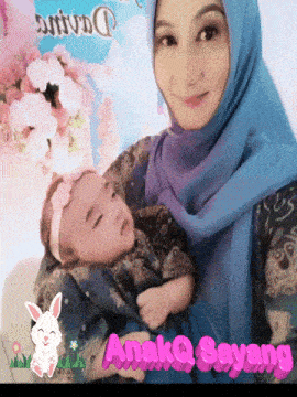 a woman in a blue hijab holds a baby in her arms with anakq sayang in pink letters