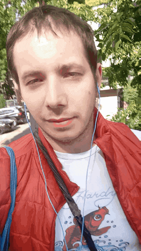 a man wearing a ed hardy shirt and a red vest takes a selfie
