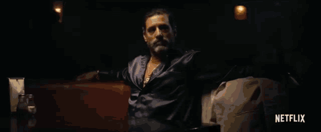 a man in a purple shirt is sitting in a dark room with a netflix logo in the corner