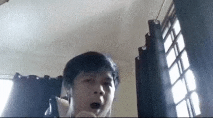 a man wearing headphones is sitting in front of a window in a room with his mouth open .
