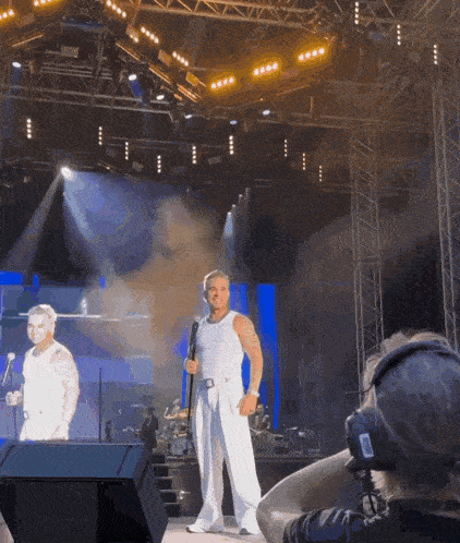 a man stands on a stage holding a microphone while a woman stands behind him