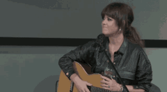 a woman is playing a guitar in front of a microphone