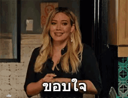 a woman in a black shirt is smiling in a kitchen with a sign in a foreign language .
