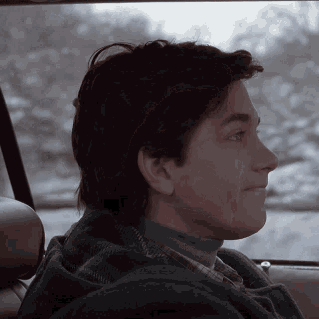 a man wearing a turtleneck and plaid shirt is sitting in the back seat of a car