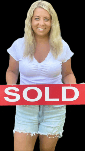 a woman is holding a sold sign in her hands