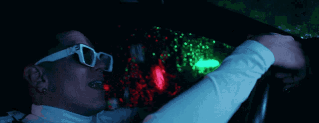 a man wearing sunglasses and a white shirt is driving