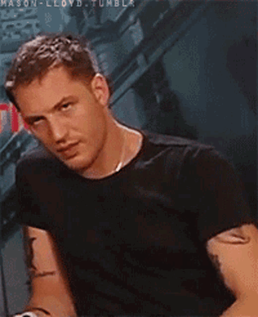 a man with a tattoo on his arm is wearing a black t-shirt