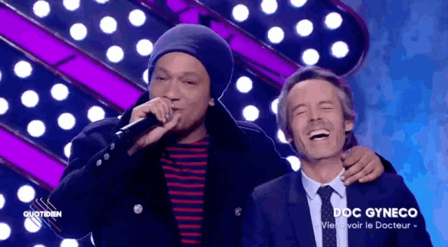 a man in a suit and tie stands next to a man singing into a microphone with the words doc gyneco on the bottom right