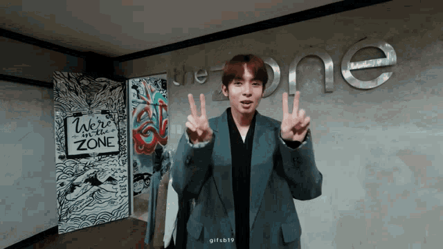 a young man giving a peace sign in front of a sign that says " we 're in the zone "