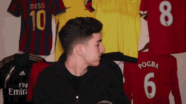 a man stands in front of a wall full of soccer jerseys including one that says pogba