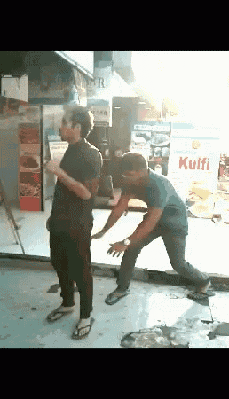 two men are dancing in front of a store that sells kulfi
