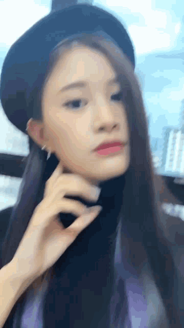 a woman wearing a black hat and a black turtleneck looks at the camera