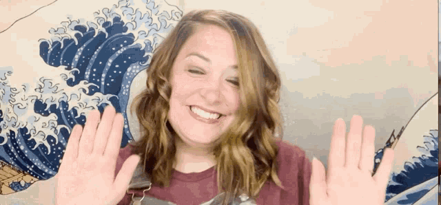 a woman smiles and waves in front of a painting of waves