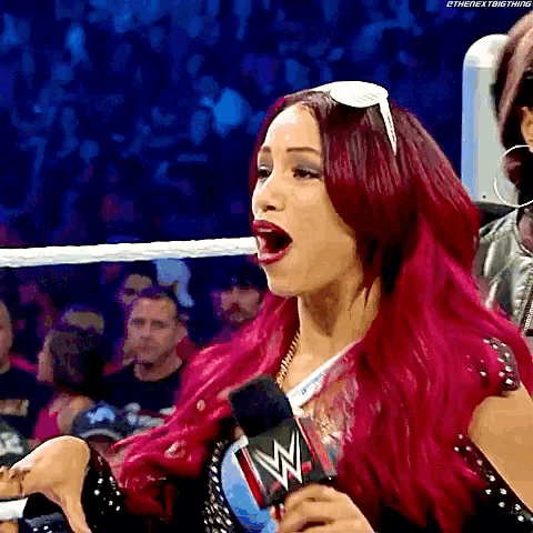 a woman with red hair is holding a microphone in a wrestling ring