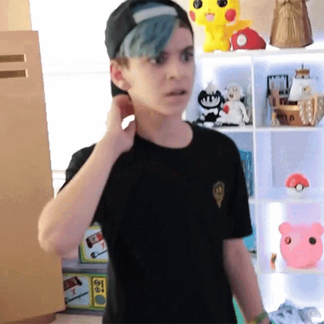 a boy with blue hair is standing in front of a shelf with stuffed animals on it