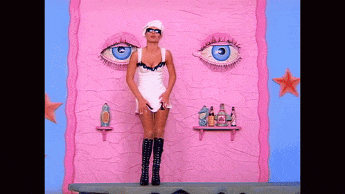 a woman in a white dress stands in front of a pink wall with large blue eyes