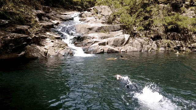 two people are swimming in a waterfall surrounded by rocks