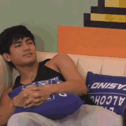 a man is sitting on a couch holding a blue pillow that says alcohol on it .