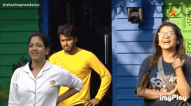 a man in a yellow shirt stands next to two women in front of a blue building
