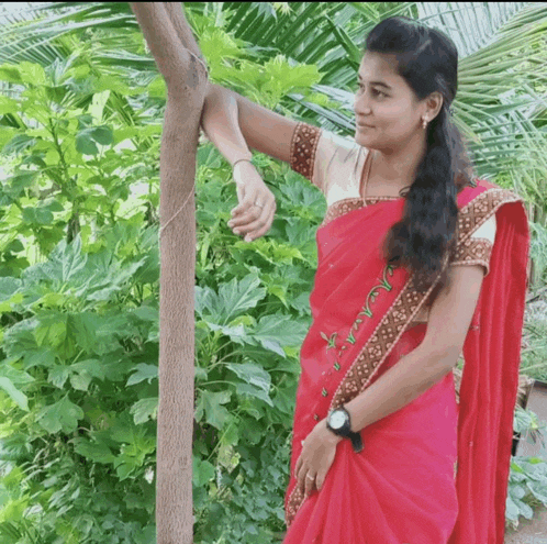a woman in a red saree stands next to a tree