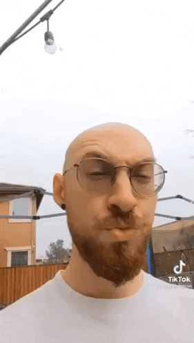 a bald man with a beard and glasses is wearing a white shirt .