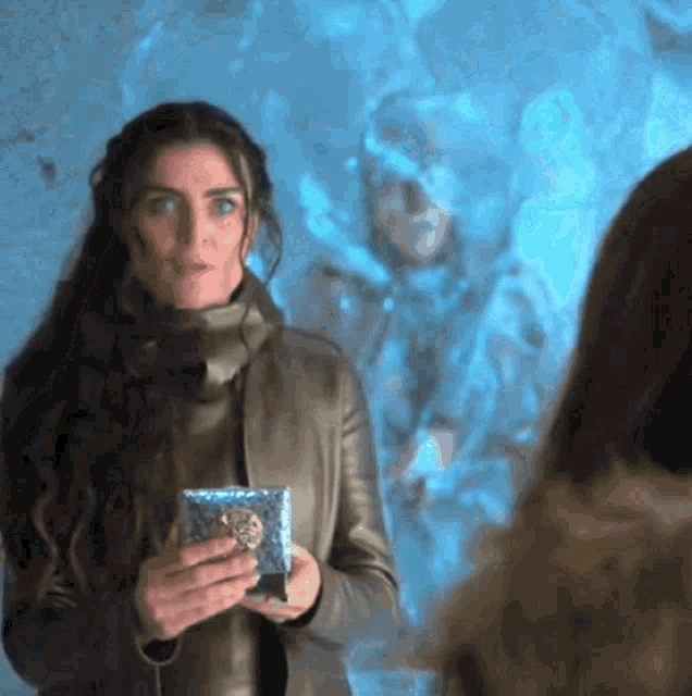 a woman in a leather jacket is holding a small blue box