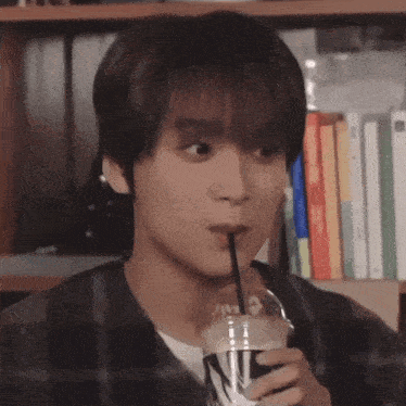 a young man drinking through a straw from a plastic cup .
